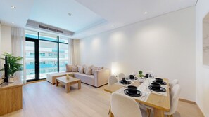 Ein modernes Wohnzimmer mit einer Couch, einem Couchtisch, einem Esstisch für vier Personen und einem großen Fenster mit Blick auf Gebäude.