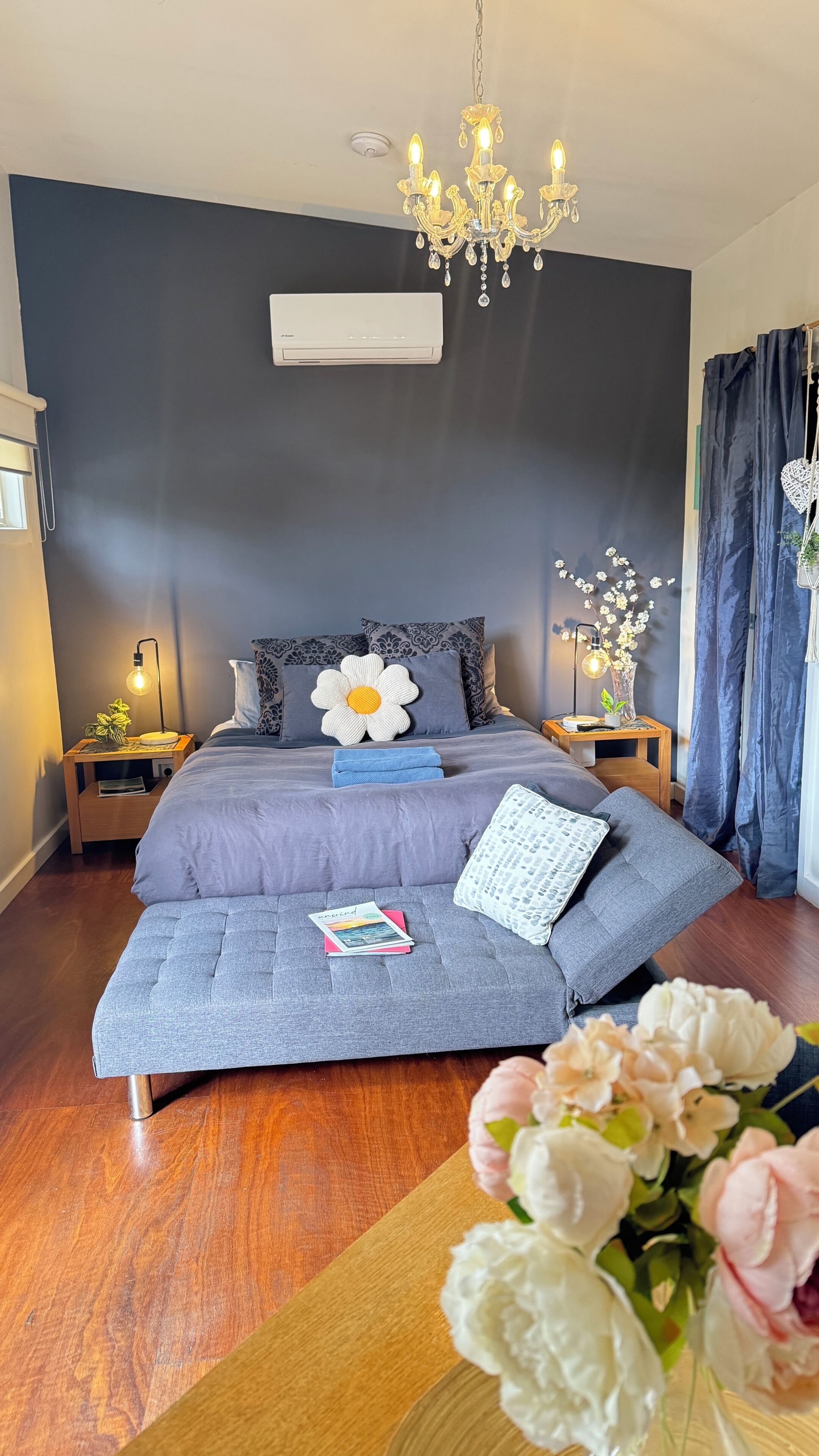 A modern bedroom with a bed, bedside tables, a chandelier, and a flower arrangement.