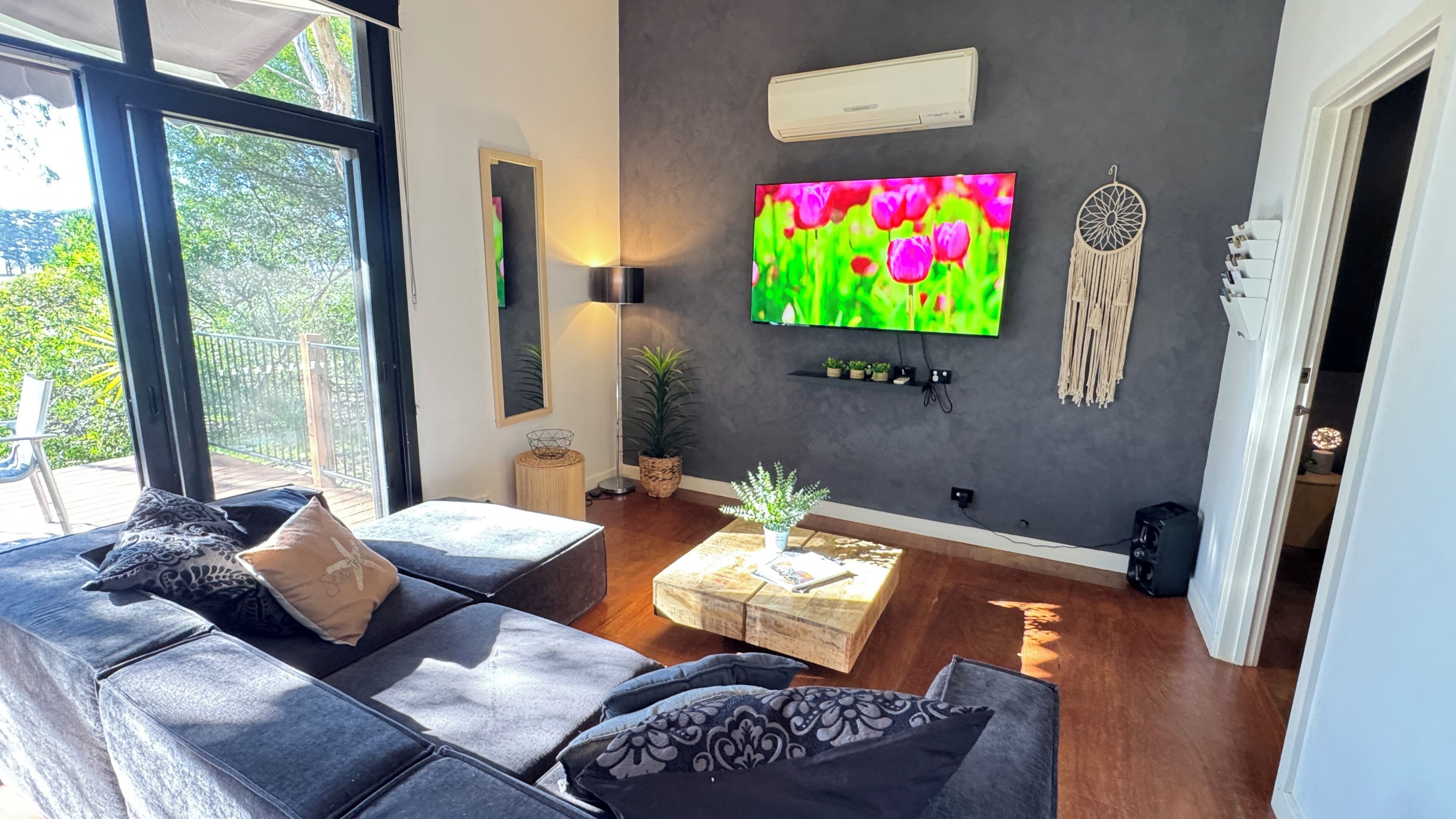 A modern living room with a grey sofa, a coffee table, a flat-screen TV, and a dreamcatcher on the wall.