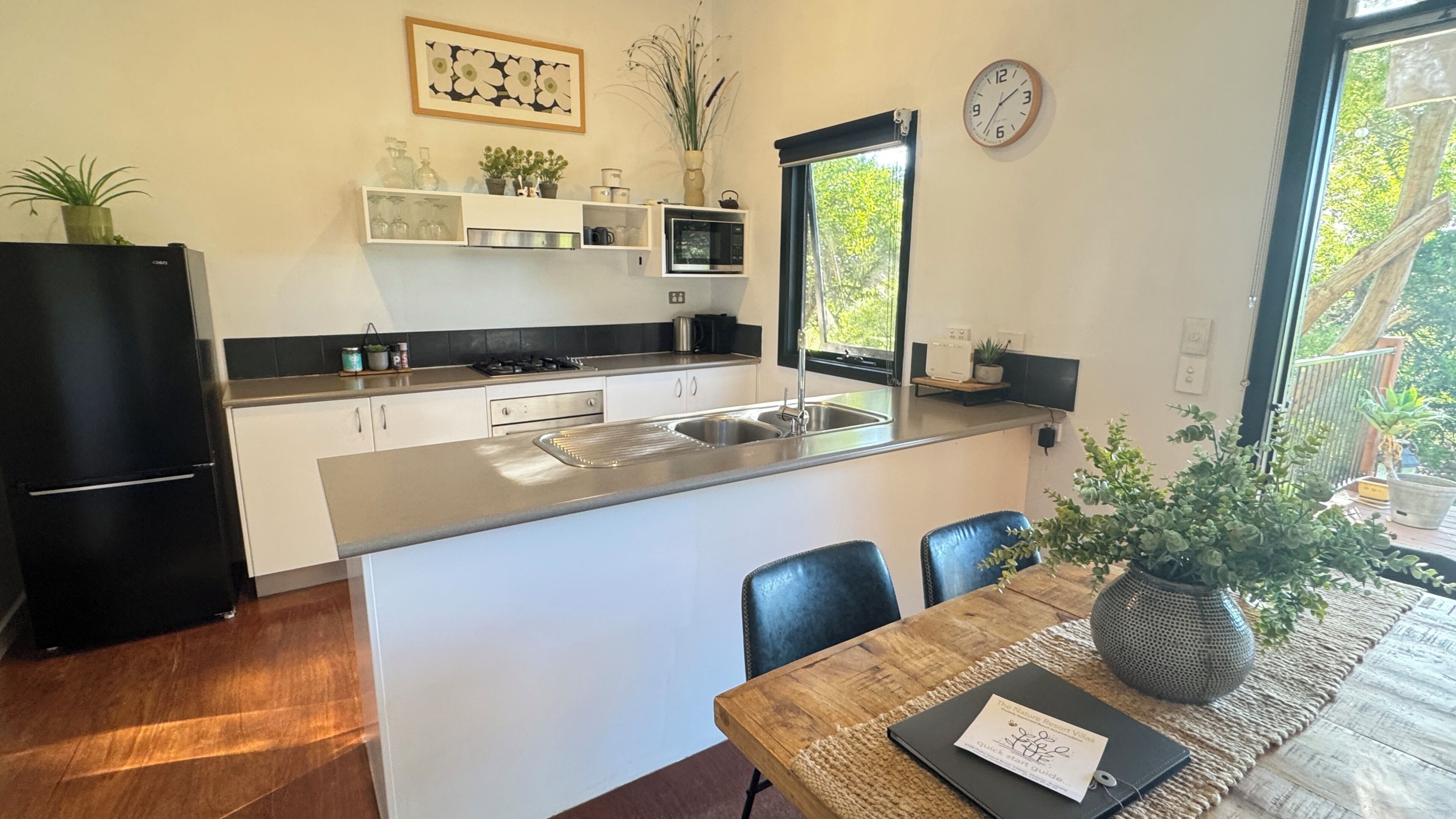 Una cocina moderna con una isla central, una mesa de comedor con sillas, un refrigerador, un microondas y un reloj en la pared.