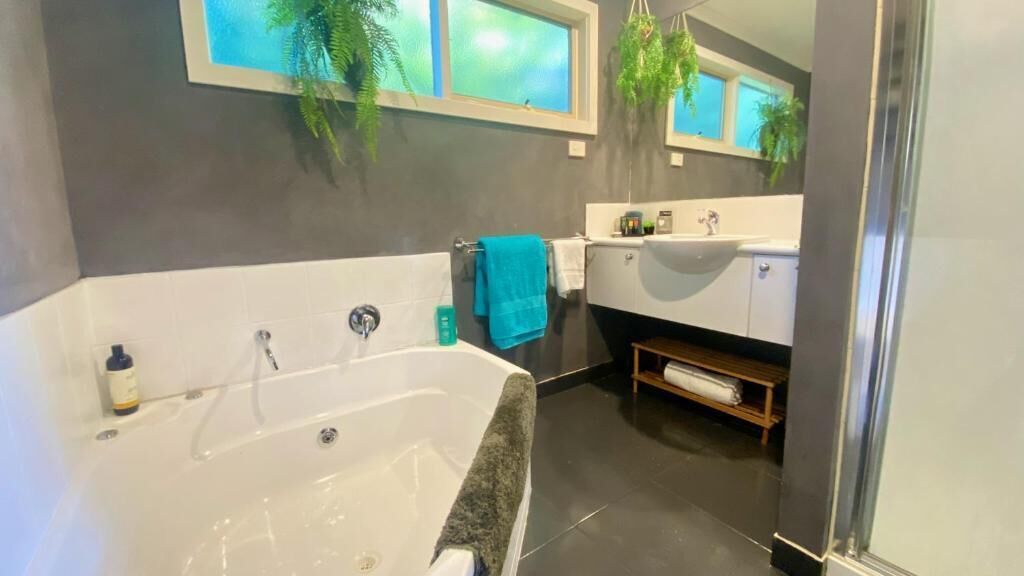 Un baño moderno con una bañera grande, un espejo sobre el lavamanos y una ventana con vista a la vegetación.