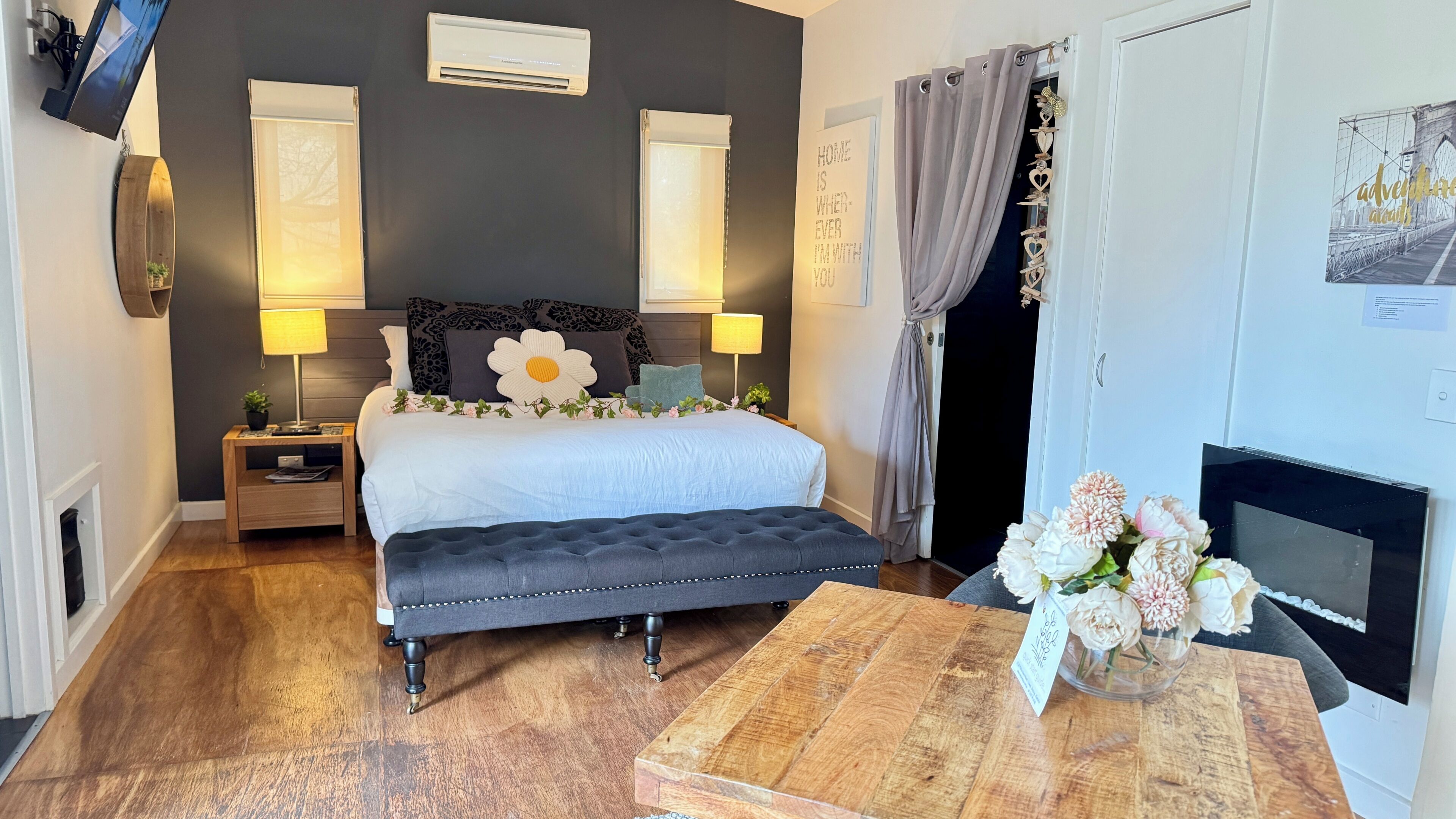A bedroom with a bed, bedside tables, a bench, a fireplace, and a TV.