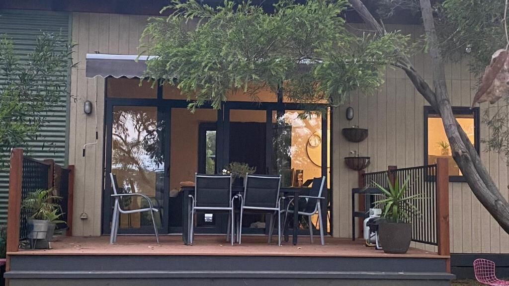 A wooden house with a covered porch, outdoor seating, and potted plants.