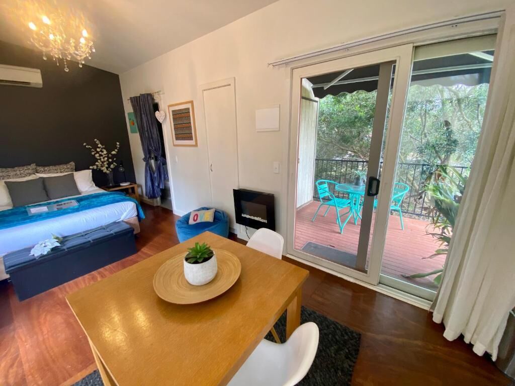 Una habitación con una cama, una mesa de madera con una planta, un televisor y una puerta corrediza de vidrio a un área exterior con sillas.