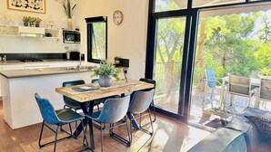 A modern kitchen with a built-in microwave, a dining area with a wooden table and blue chairs, and a large sliding glass door leading to an outdoor patio.