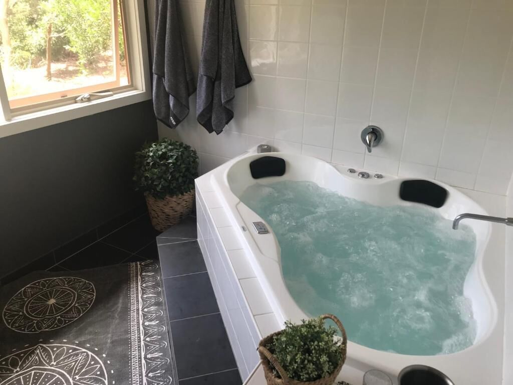 Une salle de bain avec une baignoire, une fenêtre donnant sur un beau paysage, une plante en pot et un sol carrelé.