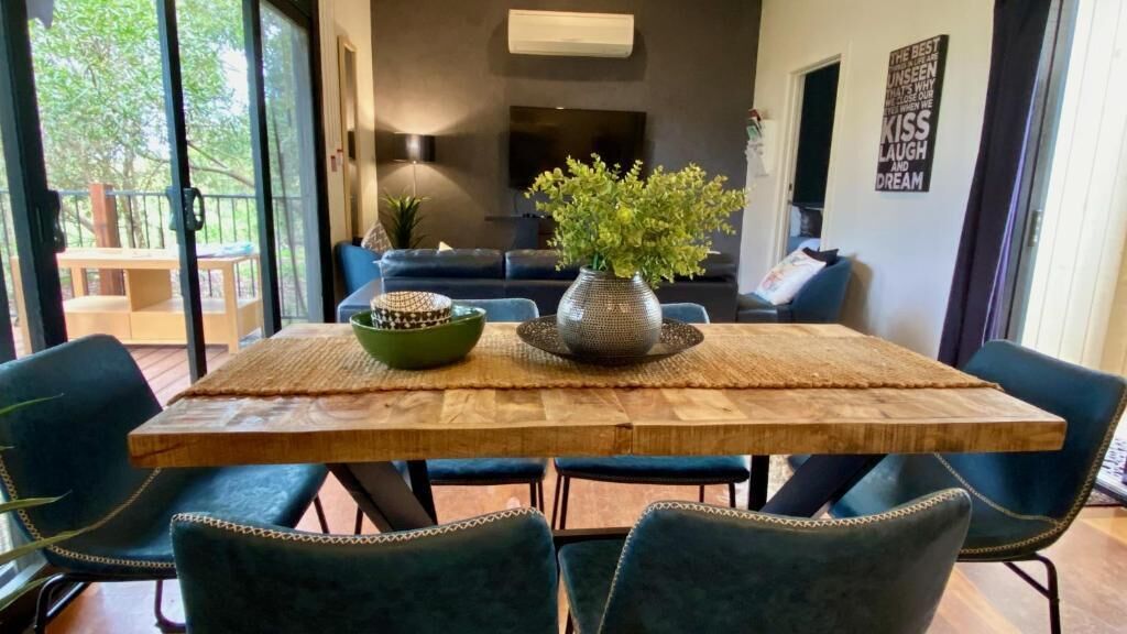A dining area with a wooden table, blue upholstered chairs, a green bowl, and a vase with green plants.