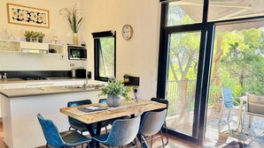 A modern kitchen with a central island, dining area with chairs, a large window, and a view of the outdoors.