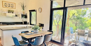Una cocina moderna con una isla central, comedor con sillas, un ventanal y vistas al exterior.
