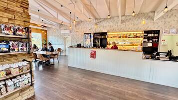 Un restaurante con área de bar, estantes de madera con aperitivos y una barra donde una persona está atendiendo.