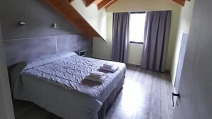 A bedroom with a bed, wooden ceiling beams, a window with curtains, and a tiled floor. - Complejo Moquehue (Villa Pehuenia)