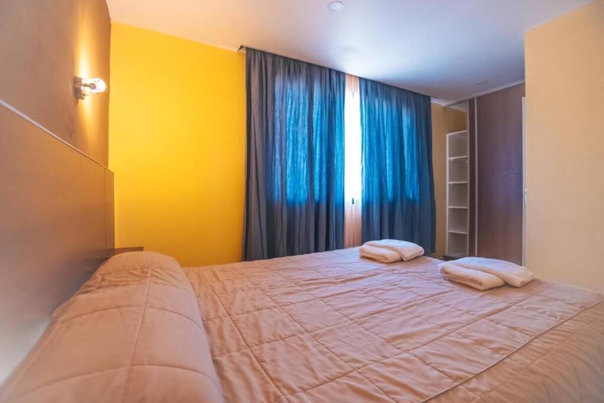 A bedroom with a bed, curtains, a wardrobe, and a shelf.