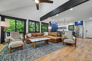 A spacious living room with a large sectional sofa, a coffee table, and a dining area with a kitchen in the background. - Designer Ski In/Out Retreat | Pool, Spa & More (Tannersville)
