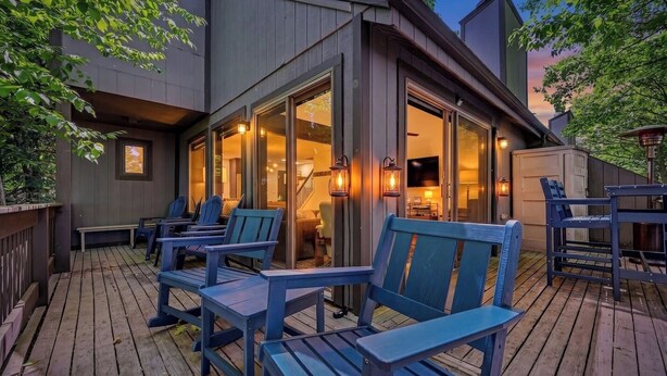 Eine Holzterrasse mit Sitzgelegenheiten im Freien, ein Glastür-Eingang und ein innenliegender Bereich mit Treppe.