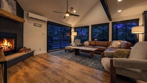 Ein Wohnzimmer mit Kamin, Deckenventilator und großem Fenster mit Blick auf eine Terrasse.