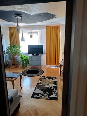 En stue med fjernsyn, trægulv, sofa, sofabord og et dekorativt tæppe.