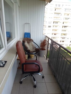 Un balcón con una silla, una mesita con una bandeja y un ventanal.