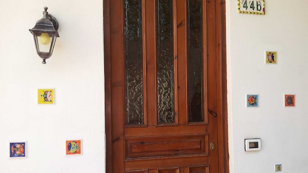 Eine Holztür mit Glasfeldern, einer Wandleuchte und mehreren kleinen, farbenfrohen Kunstwerken.