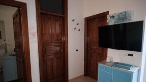Ein Zimmer mit Holztüren, einem blauen Schrank, einem an der Wand befestigten Flachbildfernseher und einem kleinen Regal mit einem weißen Gegenstand.