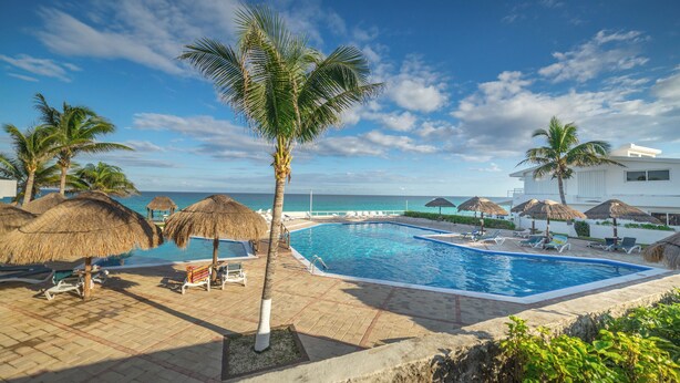 A pool area with lounge chairs, palm trees, and a view of the ocean. - Large Group Getaway - Brisas Cancun Condo 3401 (Cancún)