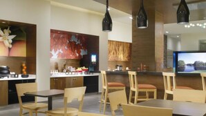 Un intérieur de restaurant moderne, avec des meubles en bois, des luminaires suspendus et un grand écran de télévision.