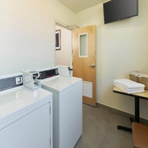 A laundry room with two washing machines, a table with folded towels, and a television mounted on the wall. - InHouse Hotel Villahermosa (Villahermosa)