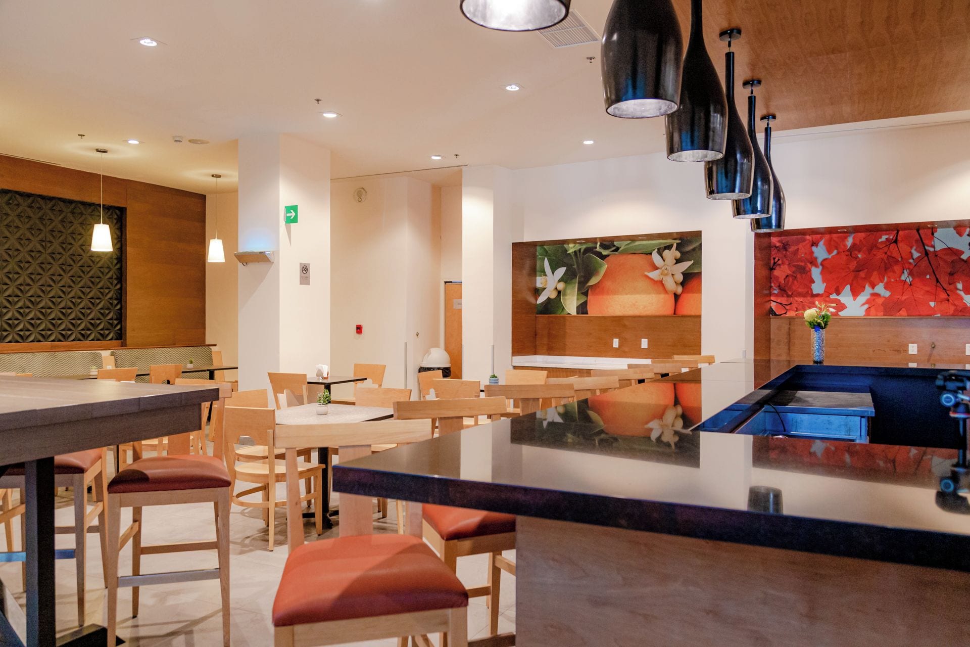 A modern restaurant interior with wooden tables and chairs, a central island with a blue countertop, and a wall with a fruit-themed mural.