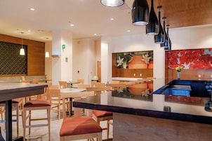A modern restaurant interior with wooden tables and chairs, a central island with a blue countertop, and a wall with a fruit-themed mural.