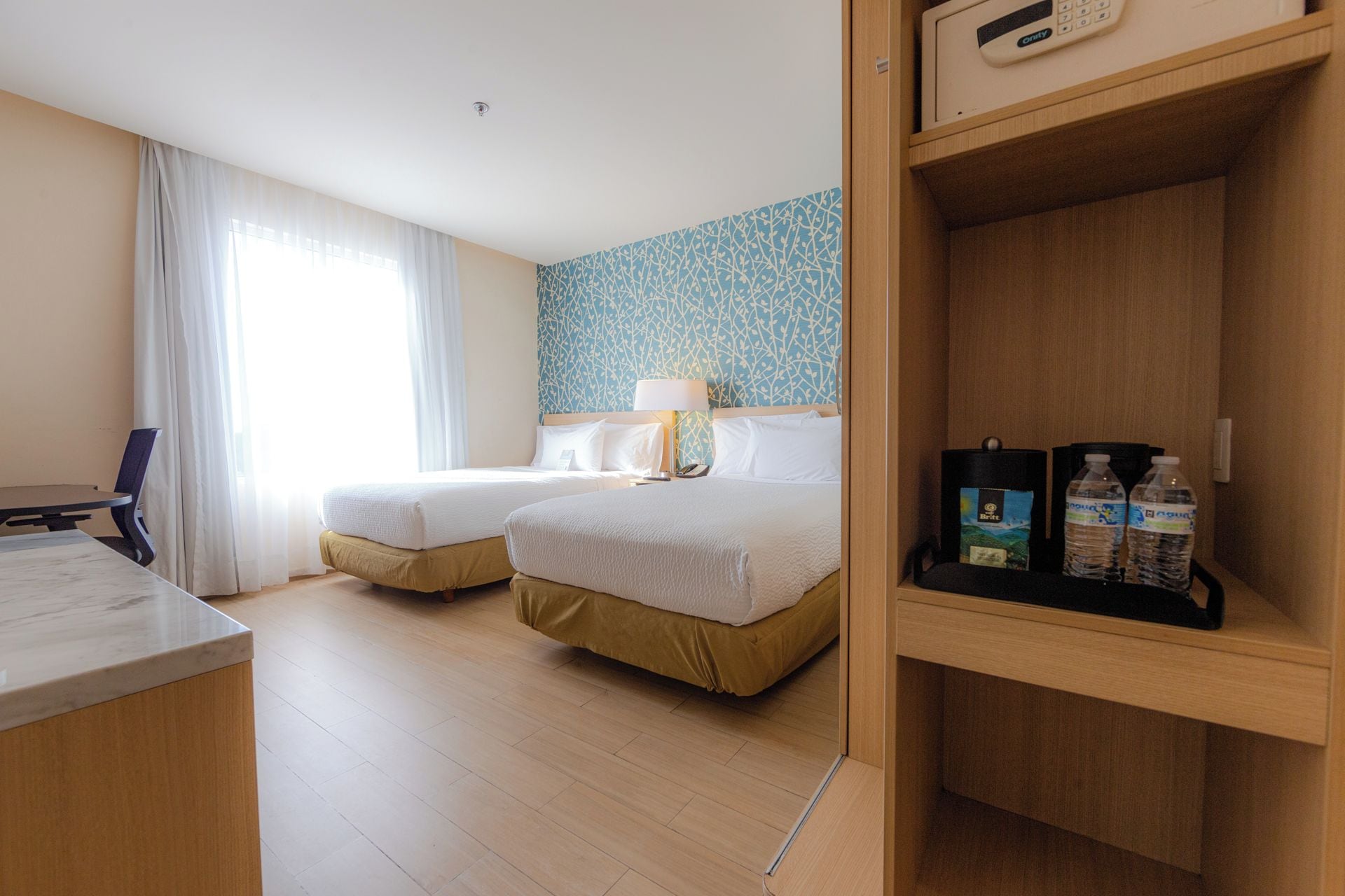 Een hotelkamer met twee bedden, een bureau, een lamp en een plank met toiletartikelen.