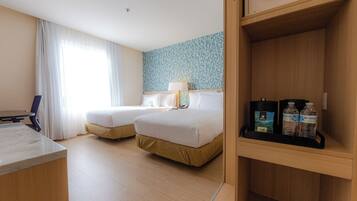 Een hotelkamer met twee bedden, een bureau, een lamp en een plank met toiletartikelen.