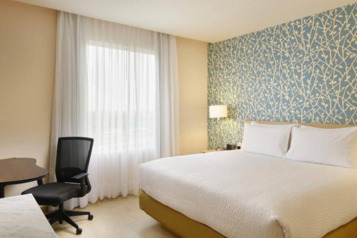 Habitación de hotel con cama, escritorio, silla, lámpara y pared con diseño.