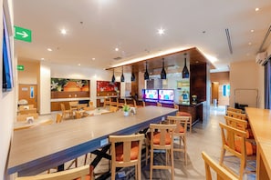 A modern restaurant with a long communal table, individual seating, and a bar area. - InHouse Hotel Villahermosa (Villahermosa)