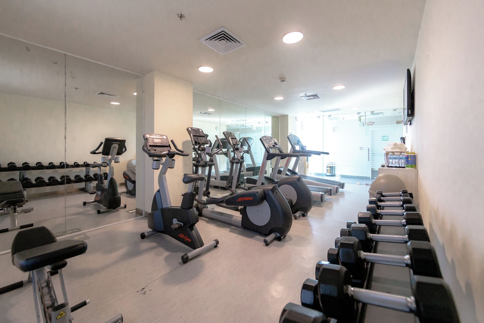 Une salle de sport équipée de divers appareils d’exercice, notamment des tapis de course, des vélos d’appartement et des haltères.