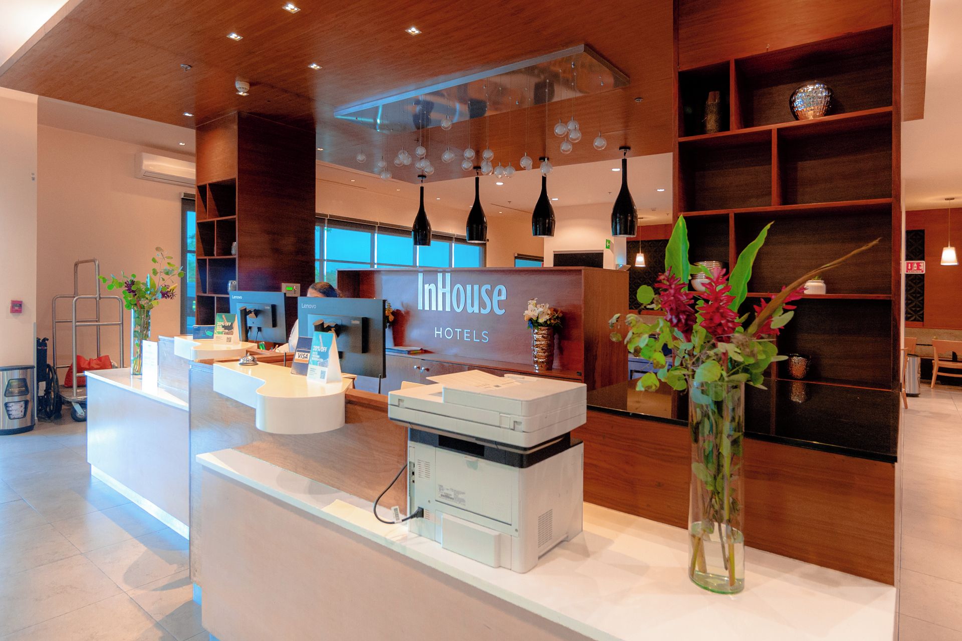 Zona de recepción de un hotel, con mostrador de recepción, estaciones de computadoras y un gran cartel que dice 'InHouse Hotels'.