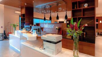 Zona de recepción de un hotel, con mostrador de recepción, estaciones de computadoras y un gran cartel que dice 'InHouse Hotels'.