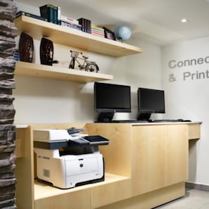 A reception desk with a printer, two monitors, and a bookshelf with books and a bicycle. - InHouse Hotel Villahermosa (Villahermosa)