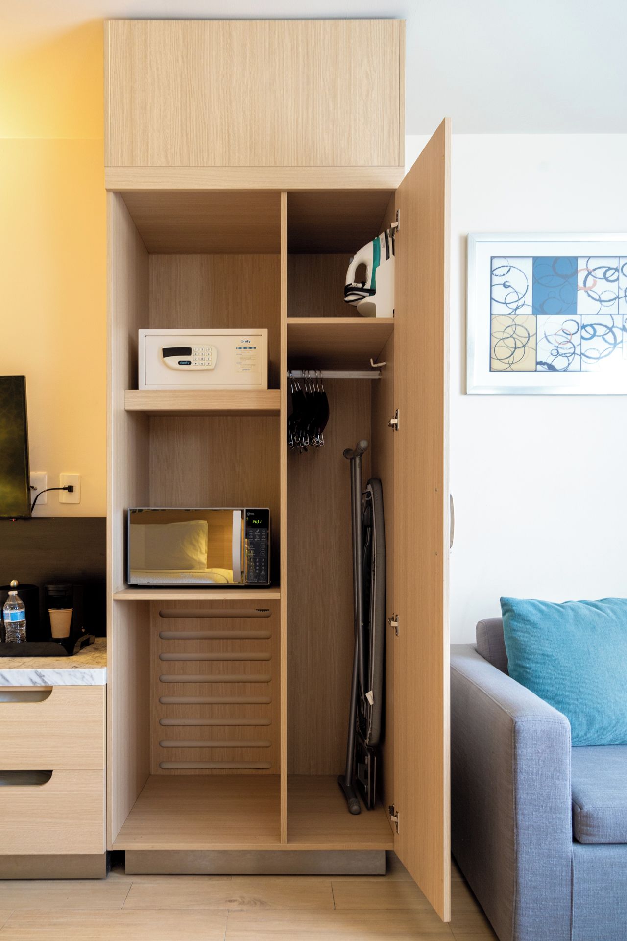 A compact living space with a wooden wardrobe, a microwave, and a vacuum cleaner.