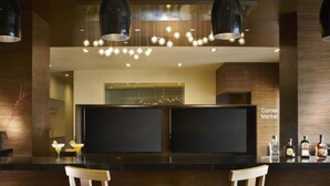 Un espace bar doté de deux grands téléviseurs à écran plat, de tabourets de bar en bois, de luminaires suspendus et d’une enseigne bien visible indiquant « Corner Market ».