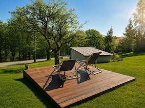 Une terrasse avec deux chaises et un petit abri de jardin, entourée d’une pelouse et d’arbres.