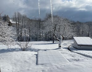 Schneebedeckte Landschaft mit Bäumen, einem Gebäude und blauem Himmel.
