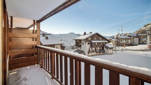 A wooden balcony with a view of a snow-covered mountain and buildings. - La Reine Blanche  (Les Belleville)