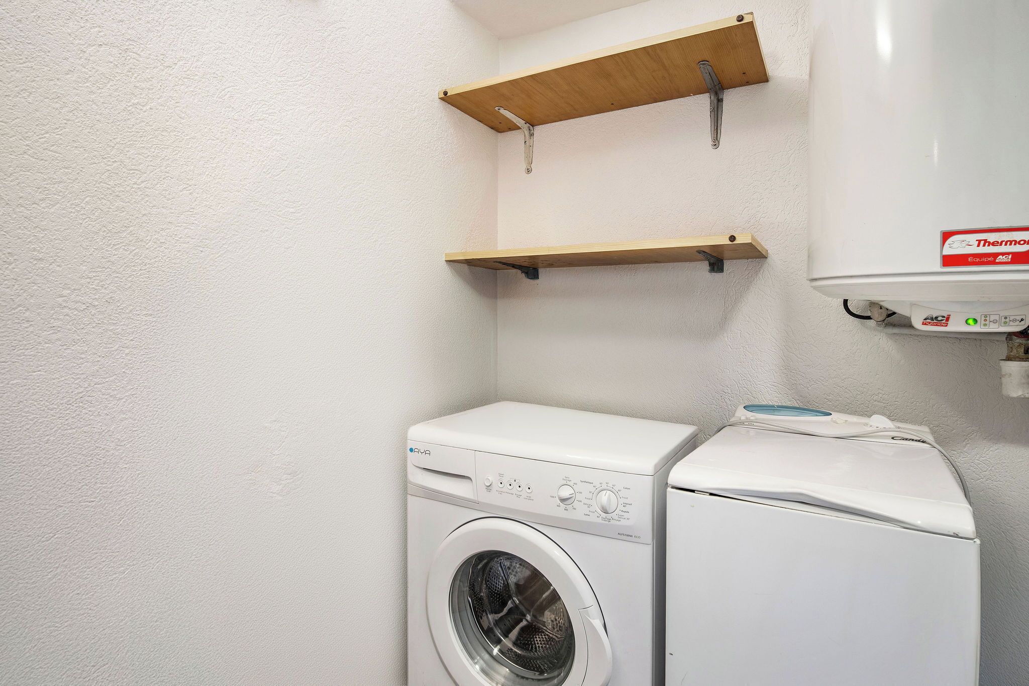 A laundry room with a front-loading washing machine and dryer, wooden shelves, and a thermostat on the wall.