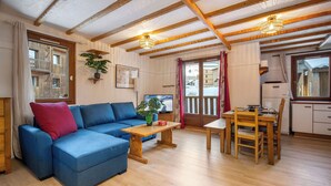 A cozy living room with a blue sofa, wooden dining table, and a kitchen area. - La Reine Blanche  (Les Belleville)