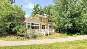 A two-story house with a covered porch and a front yard. - Cherry Bear Cottage at Woodstone in Glen Arbor (Glen Arbor)