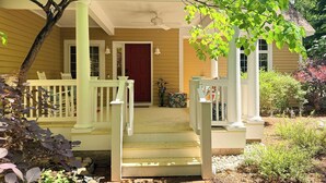 A house with a porch, a red door, and a staircase leading to the entrance. - Cherry Bear Cottage at Woodstone in Glen Arbor (Glen Arbor)