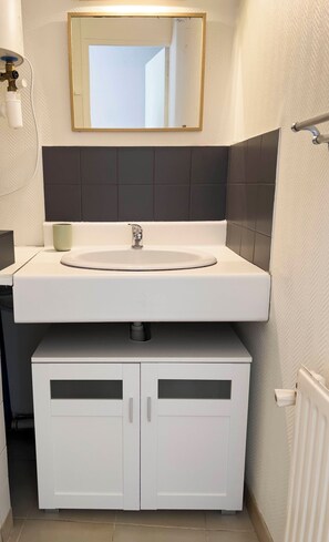Une salle de bain avec un lavabo blanc, un miroir et deux armoires.