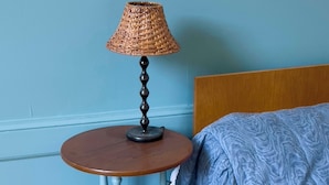 A room with a bed, a round wooden table with a lamp, and a blue wall.