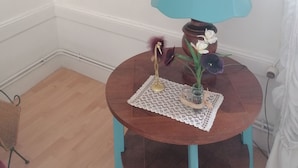 A small round table with a blue lamp, a decorative bird, and a vase with flowers.