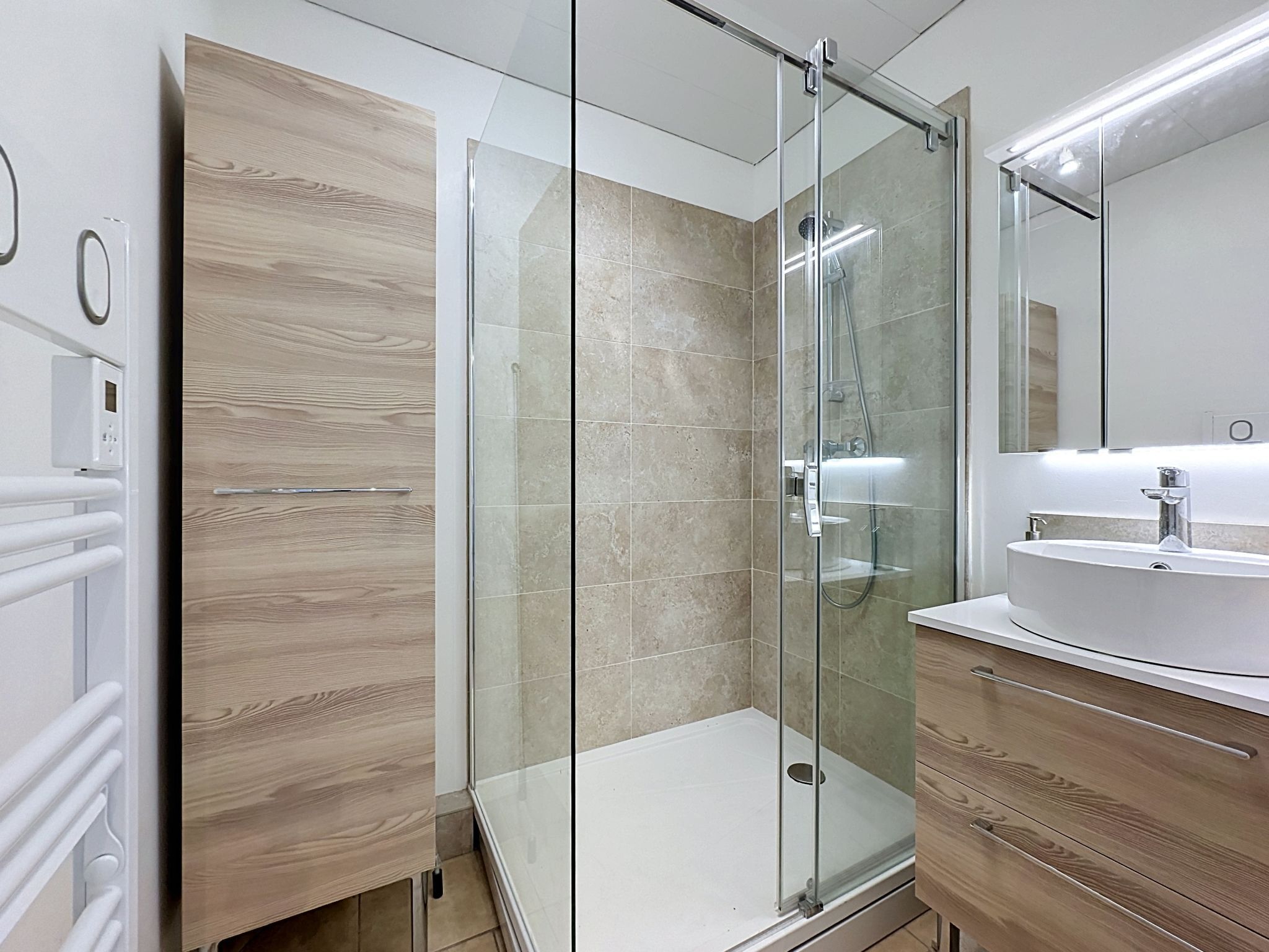 Un baño moderno con ducha de vidrio, lavamanos blanco y muebles de madera.