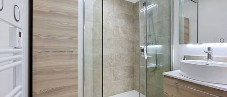 Un baño moderno con ducha de vidrio, lavamanos blanco y muebles de madera.